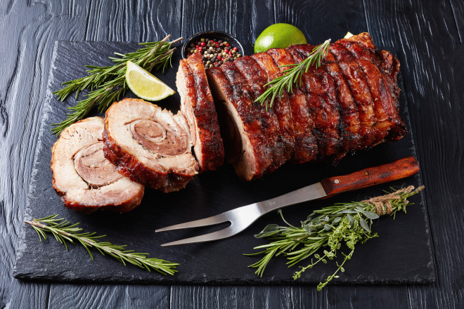 overhead view of sliced roast pork roulade -  Porchetta, delicious pork roast of Italian culinary holiday tradition on a slate tray with rosemary and lime, close-up