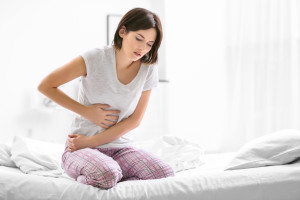 Young woman suffering from abdominal pain while sitting on bed at home