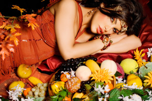 Woman laying down surrounded by fruit and flowers.