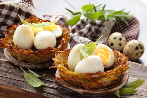 Boiled quail eggs in baked nests of potatoes. With sage and rosemary. On wooden table.