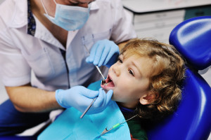 Male dentist examines the teeth of the patient cheerful child with curly red hair. Moloi boy smiling in dentist's chair. child mouth wide open in the dentist's chair