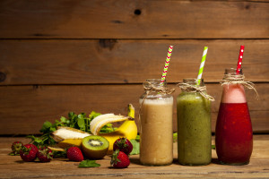 Assortment of fruit and vegetable smoothies in glass bottles with straws on wooden background.