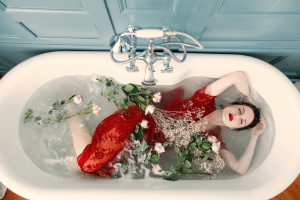 photo of beautiful young woman lying in bath full of flowers and foam and relaxing with her eyes closed