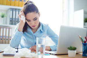 Young tired ill businesslady holding napkin in her hand and taking pills at work