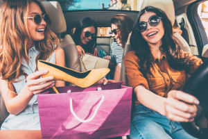 Next stop is lingerie shop! Four beautiful young cheerful women holding shopping bags and looking at each other with smile while sitting in car
