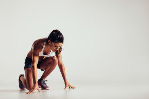 Healthy young woman preparing for a run. Fit female athlete ready for a spring over grey background with copy space.