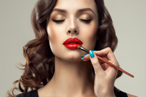 Makeup artist applies  red lipstick on lips . Beautiful woman face. Make up detail. Beauty girl with perfect skin and make-up. Red lips and nails manicure