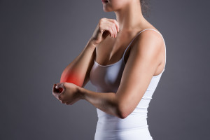 Woman with pain in elbow, joint inflammation on gray background