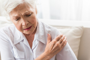 Joint pain. Senior woman is touching her arm while expressing suffering. Copy space in the right side