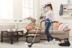 Young woman tired of spring cleaning house, washing floor with vacuum cleaner in messy room, copy space