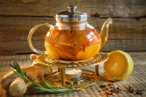 Glass tea pot with hot tasty tea with lemon, herbs,. Yellow lemon and tea. Tea pot on warm colors on wooden background. Herbal tea in a glass tea pot.
