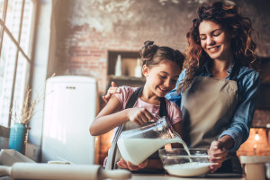 Attractive young woman and her little cute daughter are cooking on kitchen. Having fun together while making cakes and cookies.