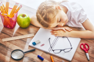 Back to school! Happy cute industrious child is sitting at a desk indoors. Kid is learning in class. Girl is tired and sleeps.