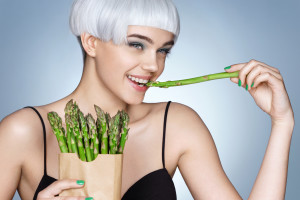 Young girl with green asparagus. Photo of smiling blonde girl on blue background. Detox concept