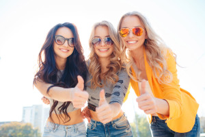 Beautiful young women,three attractive girlfriends with beautiful smiles,two blondes and a brunette,dressed in jeans and short t-shirt,spend time together in the city Park in the summer,  posing for a photograph.