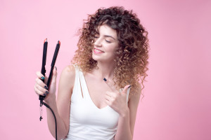 Beautiful woman with amazing curls in white shirt holds styling accessories in hand. Top view. Hair styling set with curling accessories.