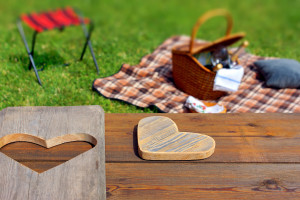 Picnic table with wooden heart blanket and basket in the grass. Background with space for text or image.
** Note: Shallow depth of field