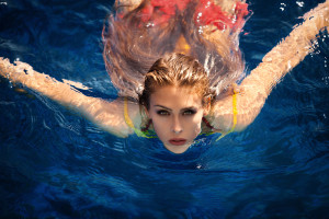 young woman in pool swimming looking at camera shot from above
