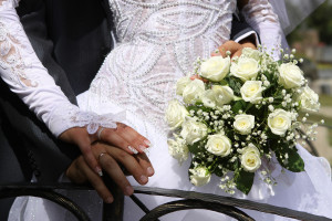 Hands of bride and groom in a heart shape on wedding bouquet