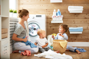 Happy family mother housewife and children in the laundry load a washing machine