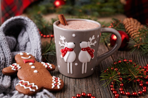 Cup of hot chocolate or cocoa with cinnamon and gingerbread man cookie in new year tree decorations frame on vintage wooden table background. Homemade traditional celebration recipe. Rustic style.
