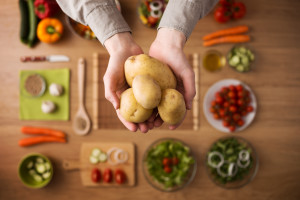Hands holding fresh harvested potatoes with raw colorful seasonal vegetables on background, top view