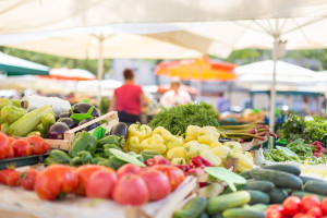 Farmers' food market stall with variety of organic vegetable. Vendor serving and chating with customers.