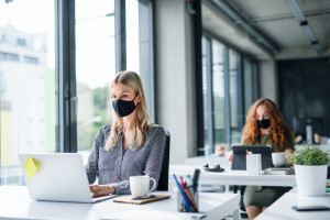 Young people with face masks back at work or school in office after lockdown.