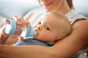 Mother, feeding her baby boy from bottle, comfortably sitting on the couch at home