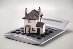 House resting on calculator concept for mortgage calculator, home finances or saving for a house