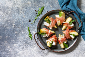 Summer snacks. Pear appetizer with jamon, arugula and brie cheese on a light stone table. Top view flat lay background. Copy space.