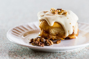 Close up of a home made cinnamon roll served on a white plate with a cream cheese frosting on top