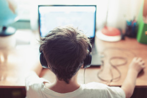 Little dependent gamer kid playing on laptop indoors