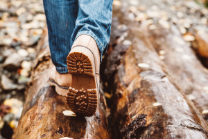 Hiker wearing boots walking across river in autumnal forest. Footwear on man's legs outdoor. Male seasonal shoes. Sole protector closeup.