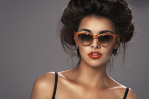 Fashion portrait of a beautiful brunette woman with shot hairstyle with orange sunglasses - studio photo