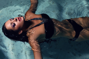 fashion photo of sexy beautiful girl with dark hair posing in swimming pool at night