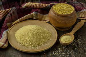 Popular ingredients oriental cuisine bulgur and couscous in a wooden pot plate and spoon checkered napkins on wooden background