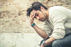 Problems and stress, stressed man. A young man with his hands in the head sitting on a bench outdoors. Concept of problems, stressful thoughts, difficulty and crisis.