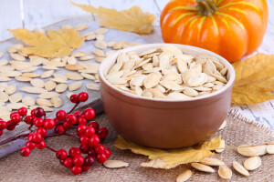 Pumpkin seeds in bowl with pumpkin on table close up