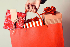 closeup of the hand of a young caucasian woman with her fingernails painted red holding a red shopping bag full of gifts wrapped in different papers