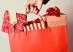 closeup of the hand of a young caucasian woman with her fingernails painted red holding a red shopping bag full of gifts wrapped in different papers