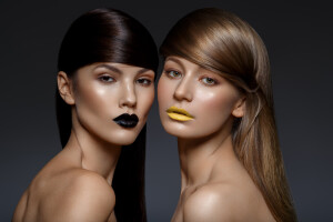 two beautiful young women with black and yellow lips and shiny healthy hair. beauty shot on black background. copy space.
