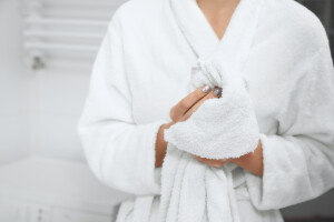 Front view close up of young woman in robe standing in bathroom with white towel after shower and wiping hands. Concept of special water procedure for care body at home.