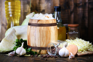 Composition with fresh and marinated cabbage (sauerkraut) in wooden barrel, on wooden table background