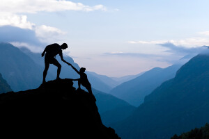Teamwork couple helping hand trust assistance silhouette in mountains sunset. Team of climbers man and woman hiker help each other on top of mountain climbing assistance beautiful sunset landscape in Himalayas Nepal