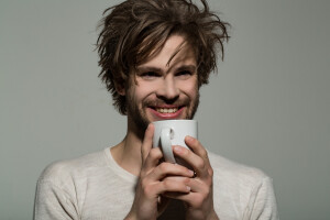 happy man with cup of tea or coffee has uncombed hair in underwear on grey background morning refreshment and drink energy