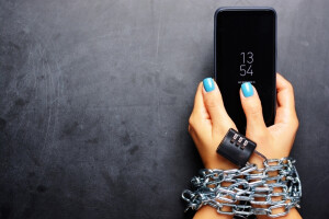 Woman hands tied with metallic chain with padlock on dark background suggesting internet or social media addiction
