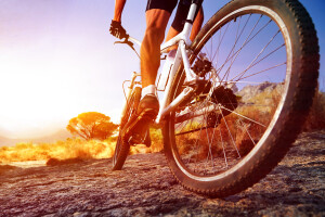 low angle view of cyclist riding mountain bike on rocky trail at sunrise