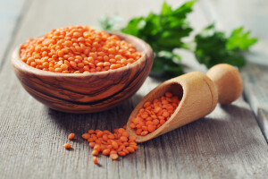 Lentils in wooden bowl with scoop on wooden background closeup